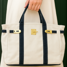 Load image into Gallery viewer, “Boatkin” Canvas Tote Bag w/ Gold Buckle Hardware - ivory with navy trim
